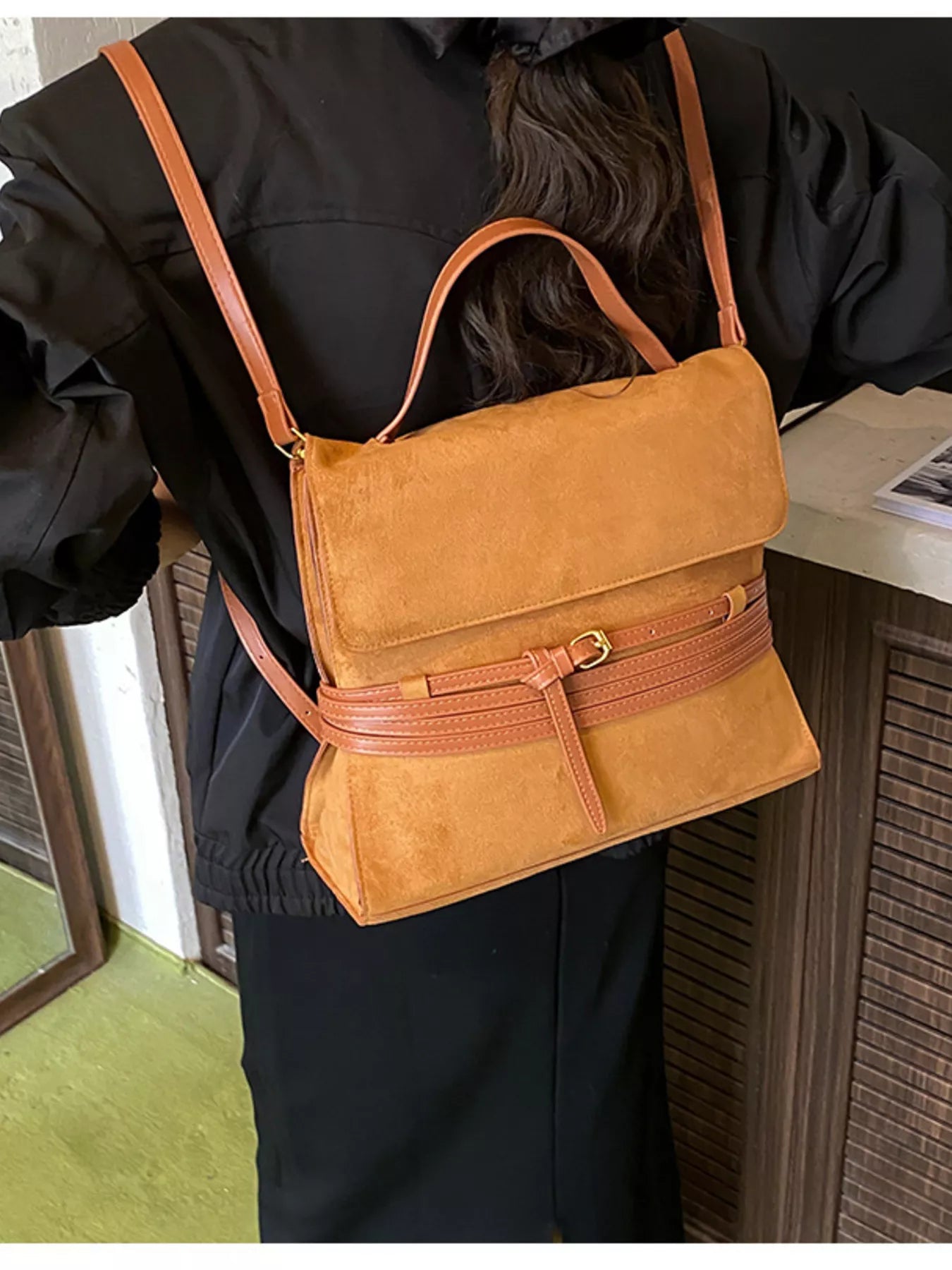 Person wearing a tan leather crossbody bag with brown straps indoors.