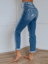 Person wearing distressed blue jeans standing on a wooden floor with a white wall background