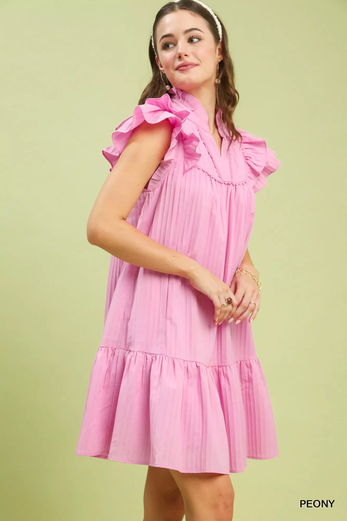 Woman wearing a pink dress with ruffled sleeves on a light green background