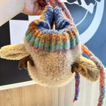 Plush toy with a colorful sweater held by a hand against a blurred background