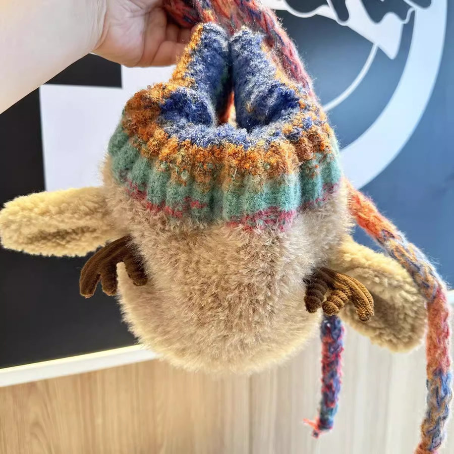 Plush toy with a colorful sweater held by a hand against a blurred background