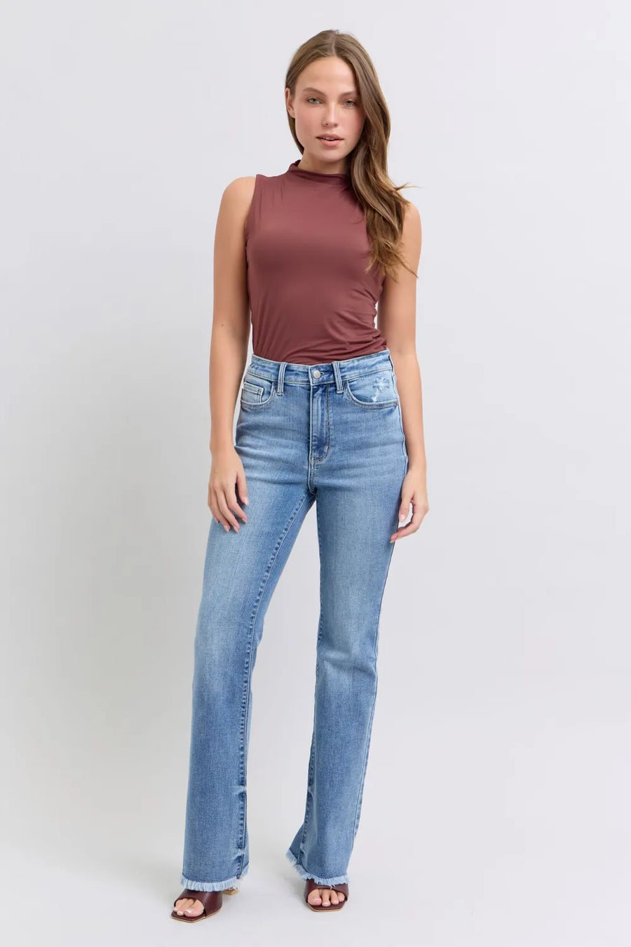 Woman wearing a brown sleeveless top and blue jeans on a white background