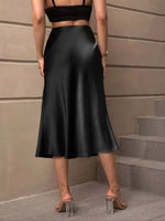 Person wearing a black satin skirt standing on steps with a neutral wall background