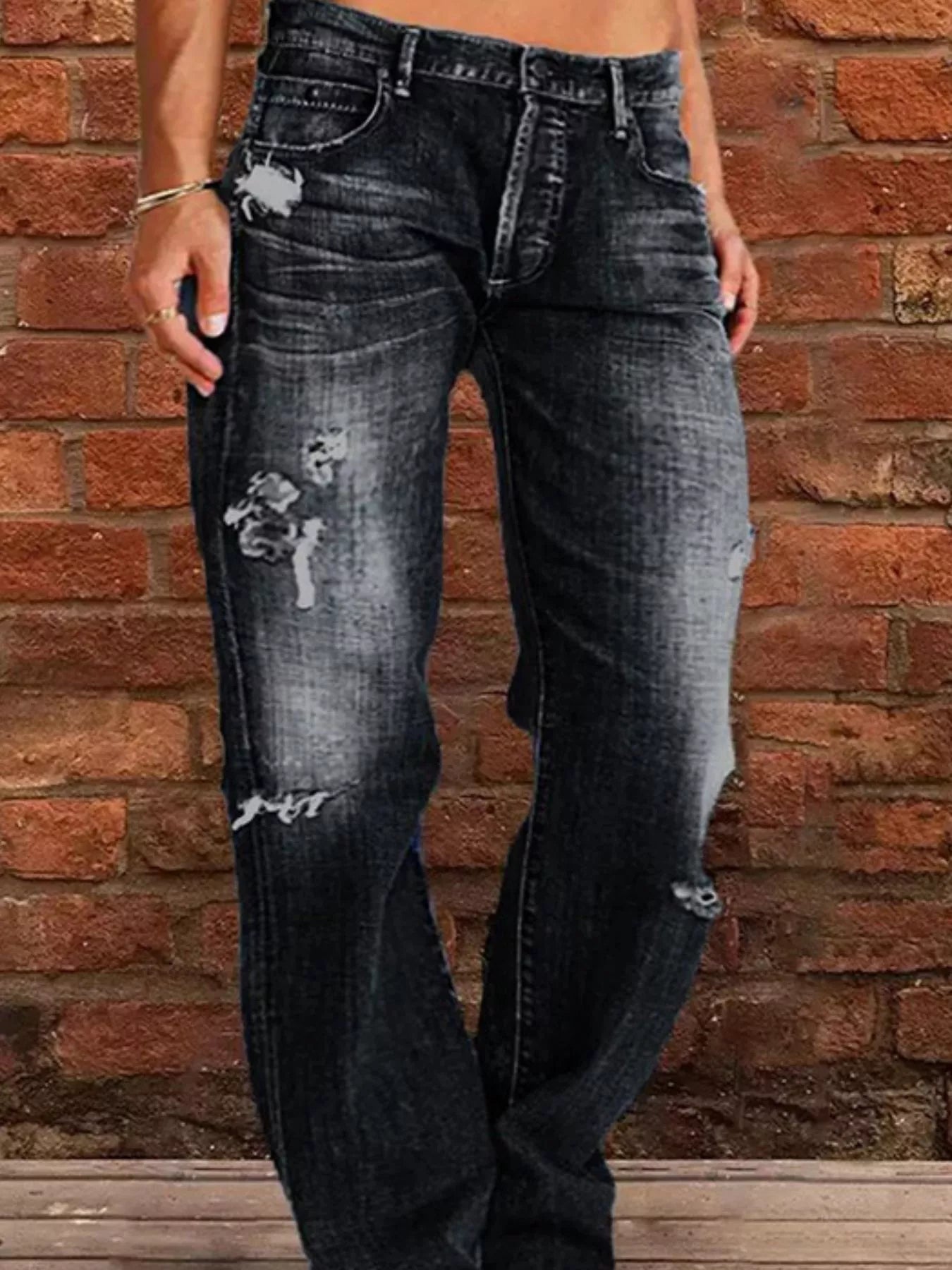 Person wearing distressed black jeans against a brick wall.