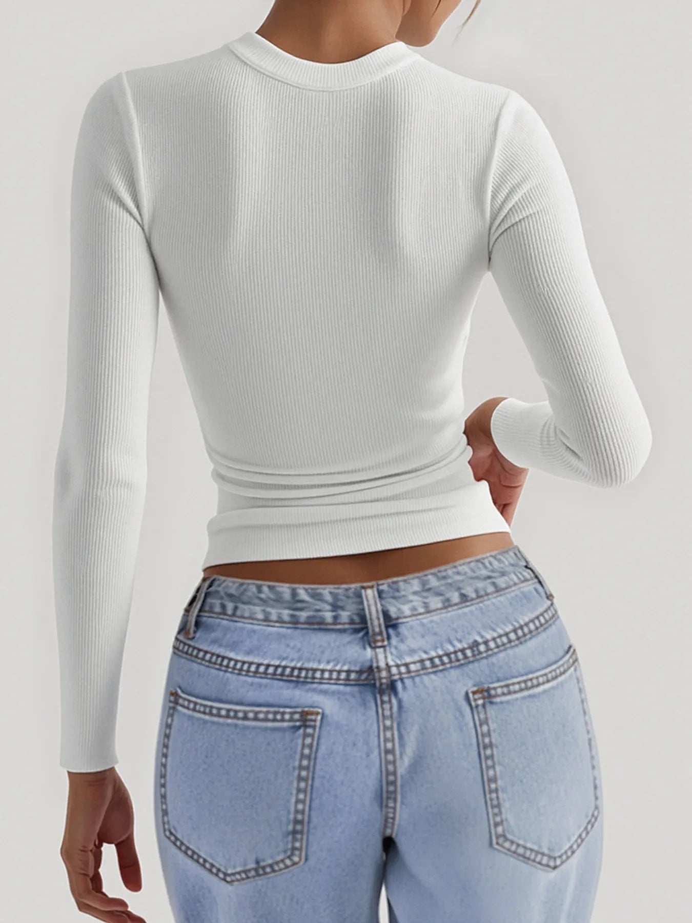 Person wearing a white long-sleeve crop top and light blue jeans on a plain background