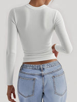 Person wearing a white long-sleeve crop top and light blue jeans on a plain background