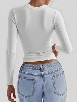 Person wearing a white long-sleeve crop top and light blue jeans on a plain background