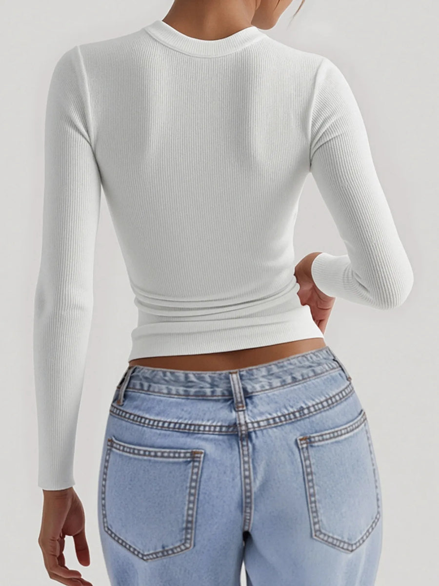 Person wearing a white long-sleeve crop top and light blue jeans on a plain background
