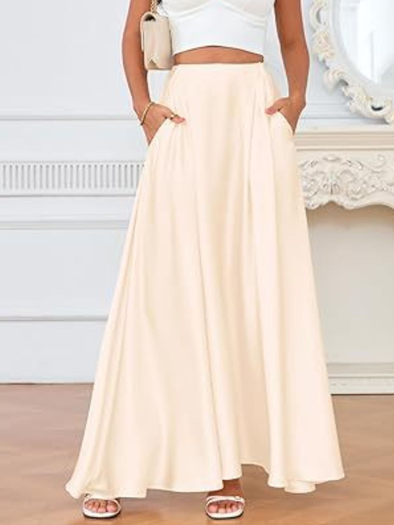 Person wearing a long beige skirt with a white top in an indoor setting.