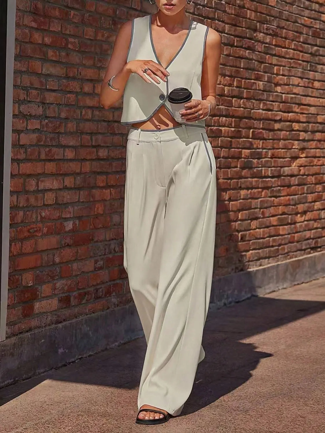 Person wearing a sleeveless top and wide-leg pants against a brick wall.