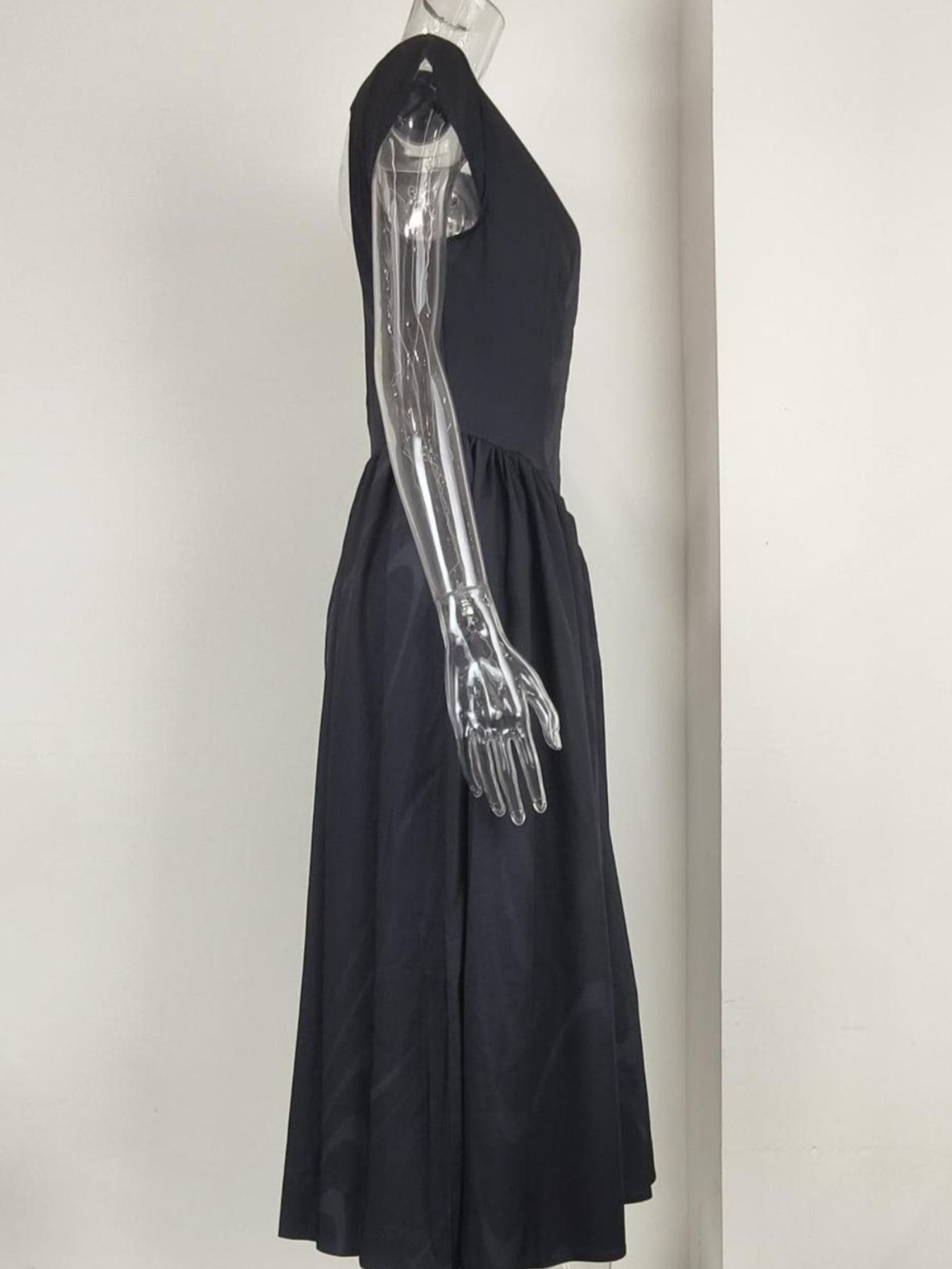 Black dress with a metallic arm on a mannequin against a plain background