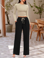 Woman wearing a light green long-sleeve top and black wide-leg pants in an indoor setting.