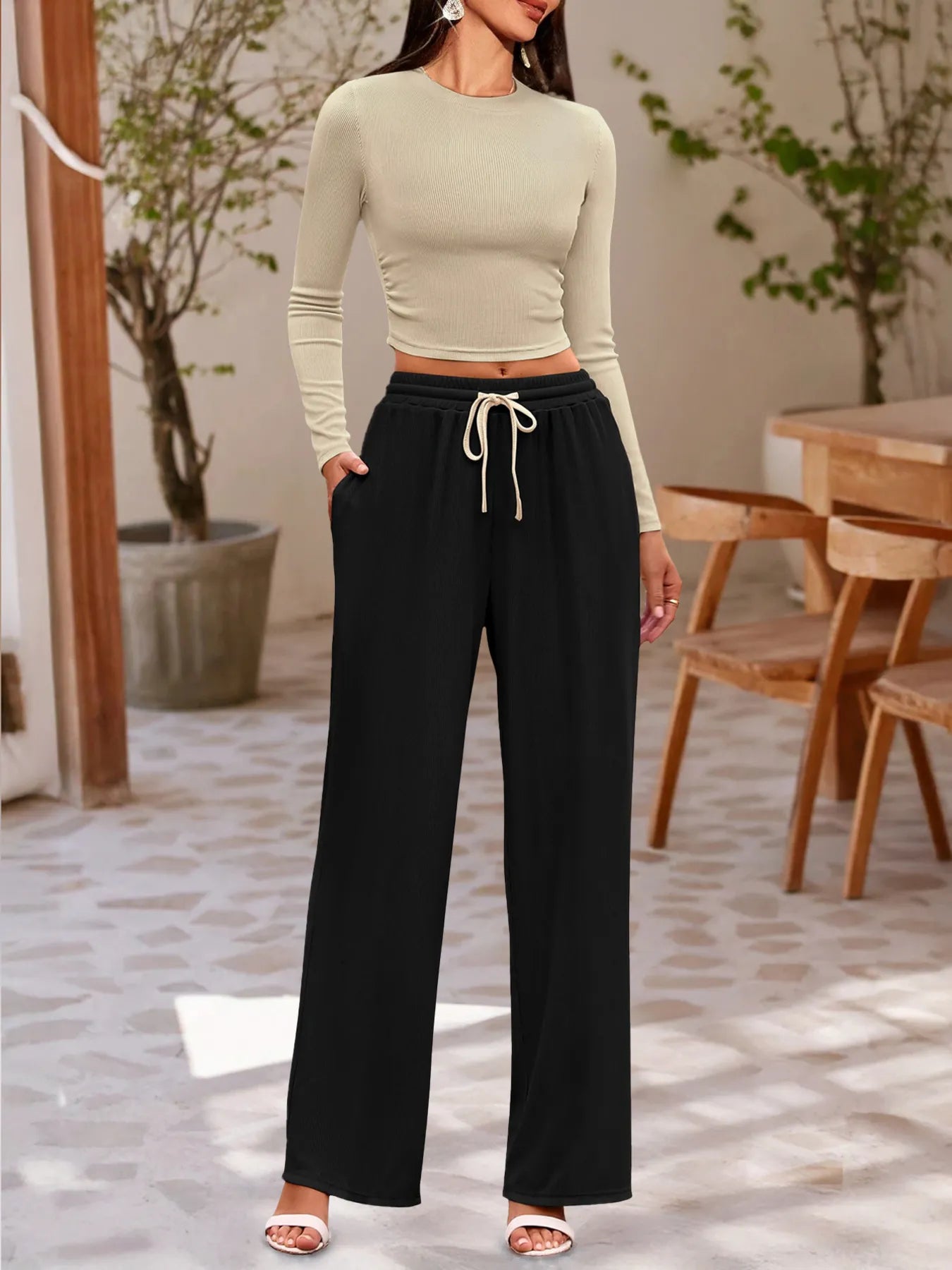 Woman wearing a light green long-sleeve top and black wide-leg pants in an indoor setting.