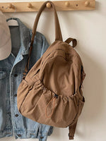 Brown backpack hanging on a wooden hook with a denim jacket and beige cap in the background.