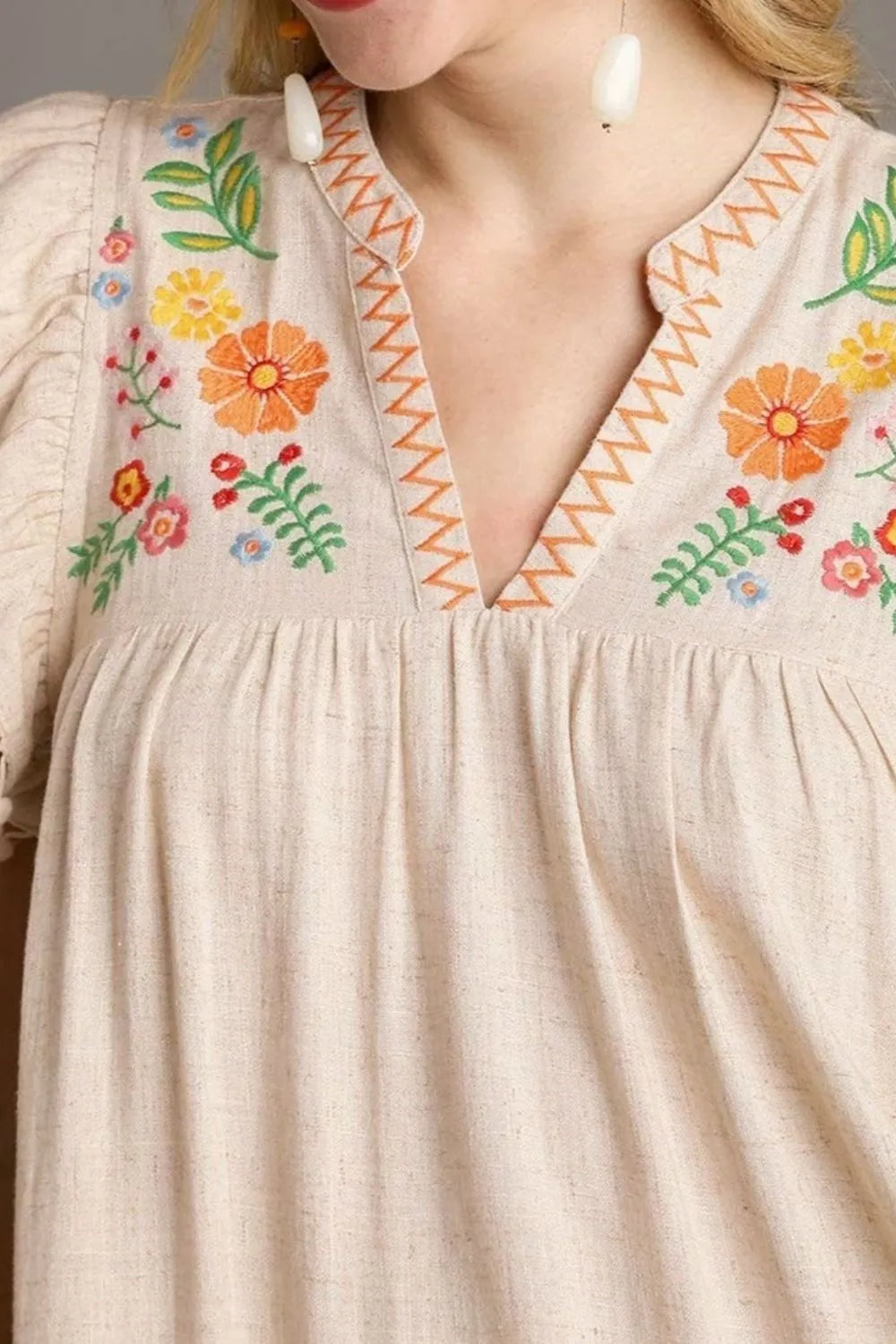 Beige dress with colorful floral embroidery on a plain background