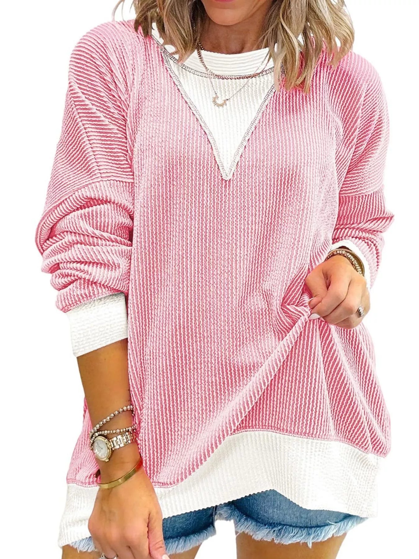 Pink textured sweater over a white shirt with denim shorts on a white background