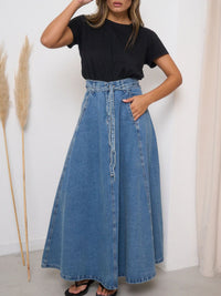Person wearing a black t-shirt and blue denim skirt against a white wall.