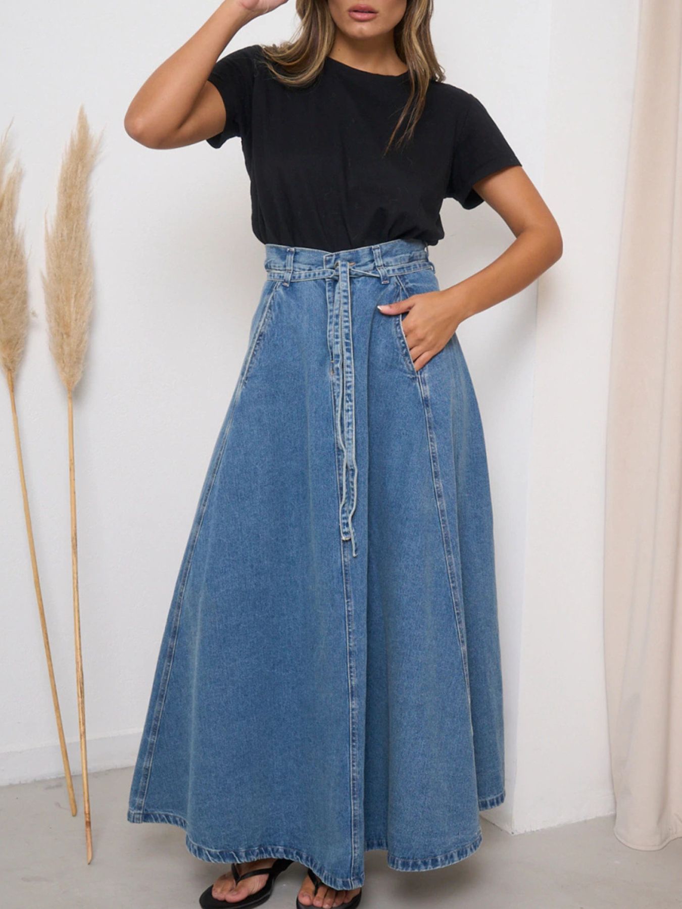 Person wearing a black t-shirt and blue denim skirt against a white wall.