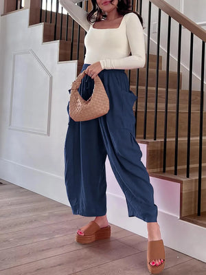 Woman in a white top and blue pants holding a woven handbag on a wooden floor.