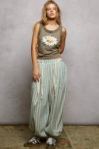 Woman wearing a tank top with a floral design and striped pants against a plain background