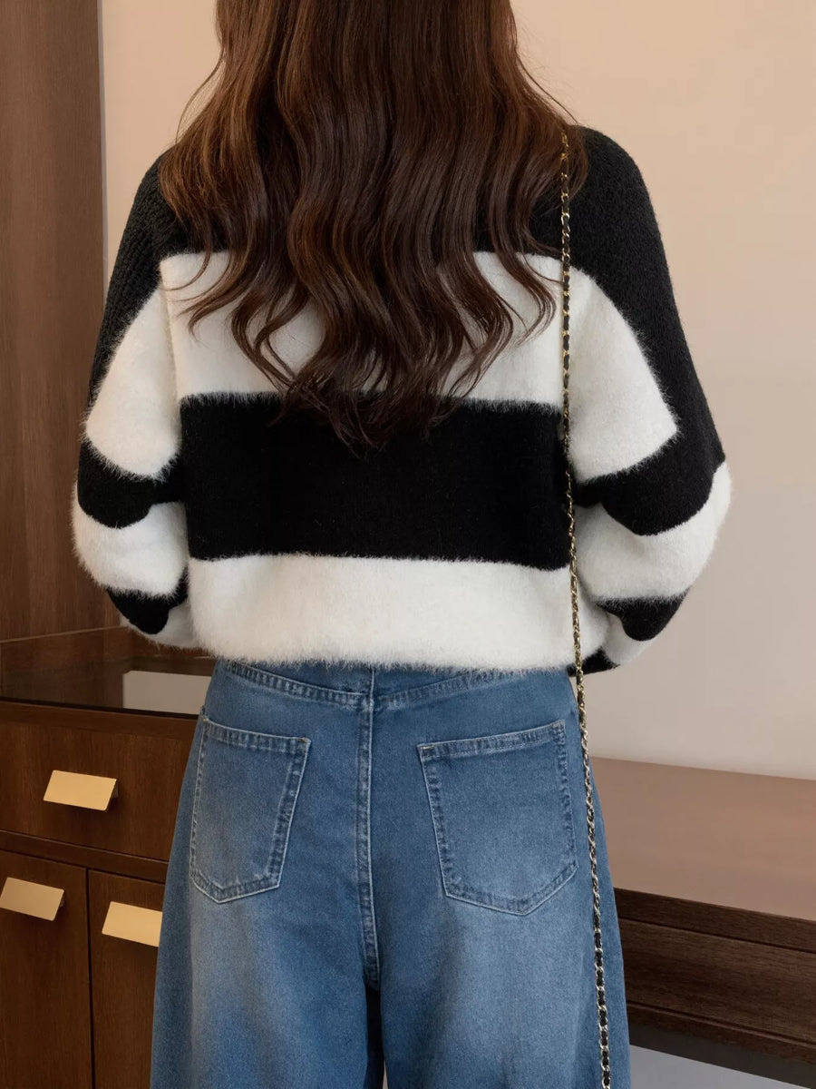 Person wearing a black and white striped sweater and blue jeans in an indoor setting.