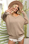 Woman wearing a beige sweater and hat, making a peace sign in front of cacti.