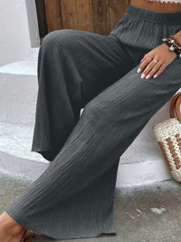 Person wearing gray wide-leg pants sitting on a stone step.