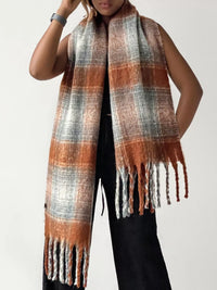 Person wearing a plaid scarf with orange, gray, and white colors on a plain background