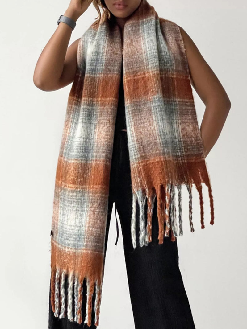 Person wearing a plaid scarf with orange, gray, and white colors on a plain background