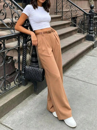 Person wearing a white top and tan pants standing on a sidewalk.