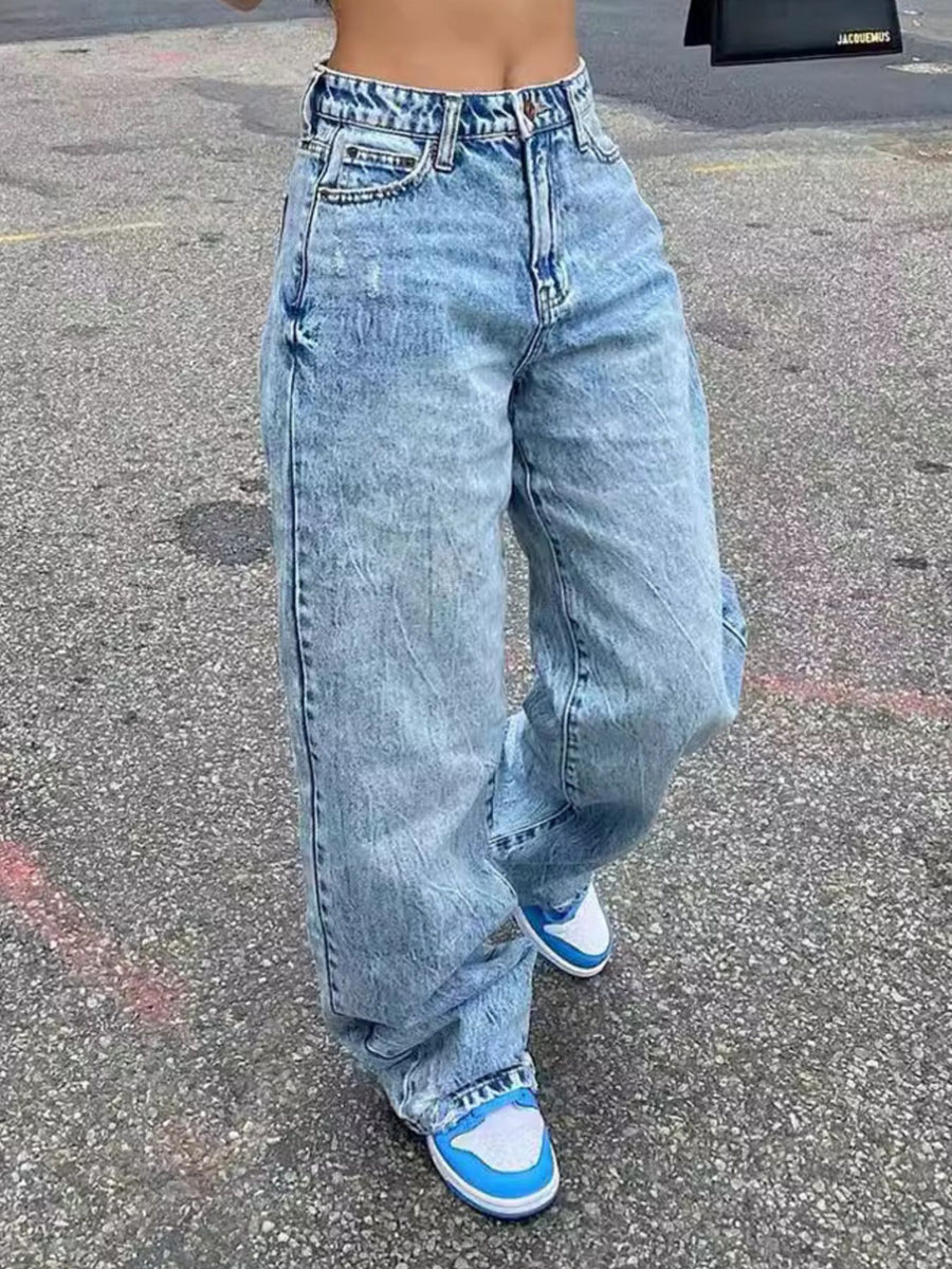 Person wearing light blue jeans and blue sneakers on a concrete surface