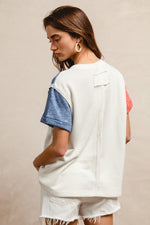 Woman wearing a white oversized shirt with blue sleeves and denim shorts on a beige background