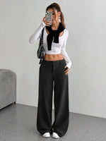 Person wearing a white long-sleeve top with a black scarf and black wide-leg pants, standing against a plain background.