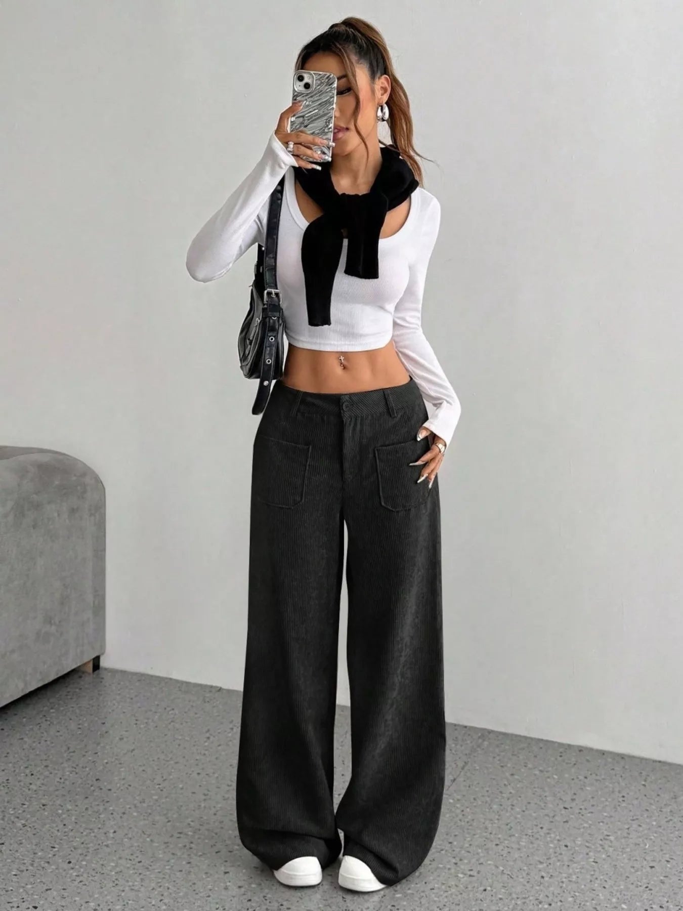 Person wearing a white long-sleeve top with a black scarf and black wide-leg pants, standing against a plain background.
