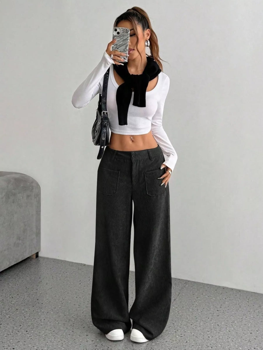 Person wearing a white long-sleeve top with a black scarf and black wide-leg pants, standing against a plain background.