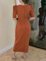 Woman wearing a rust-colored dress with puff sleeves in an indoor setting.
