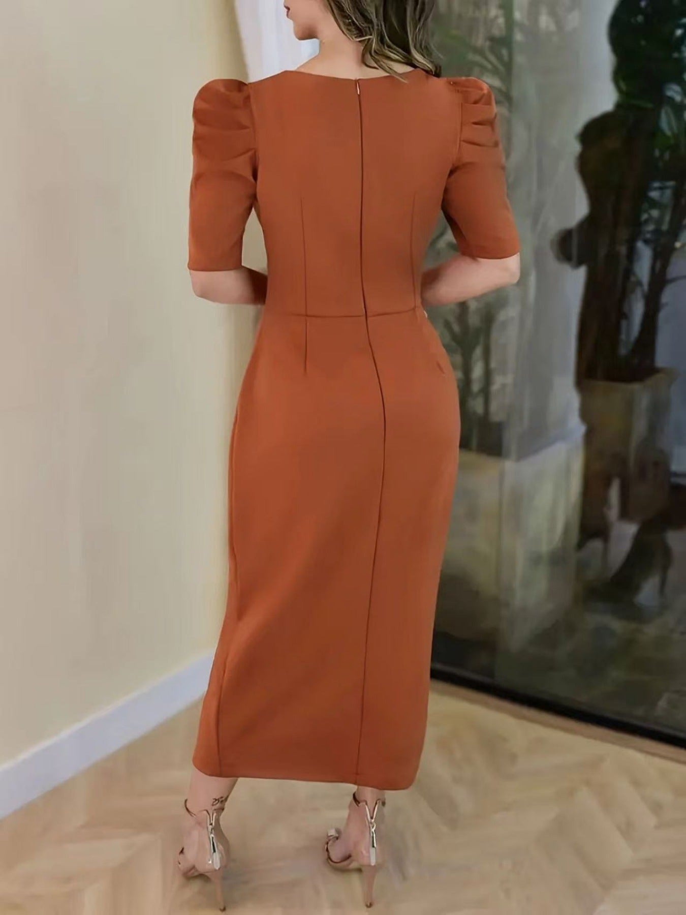 Woman wearing a rust-colored dress with puff sleeves in an indoor setting.