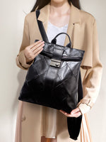 Person holding a black leather backpack against a neutral background