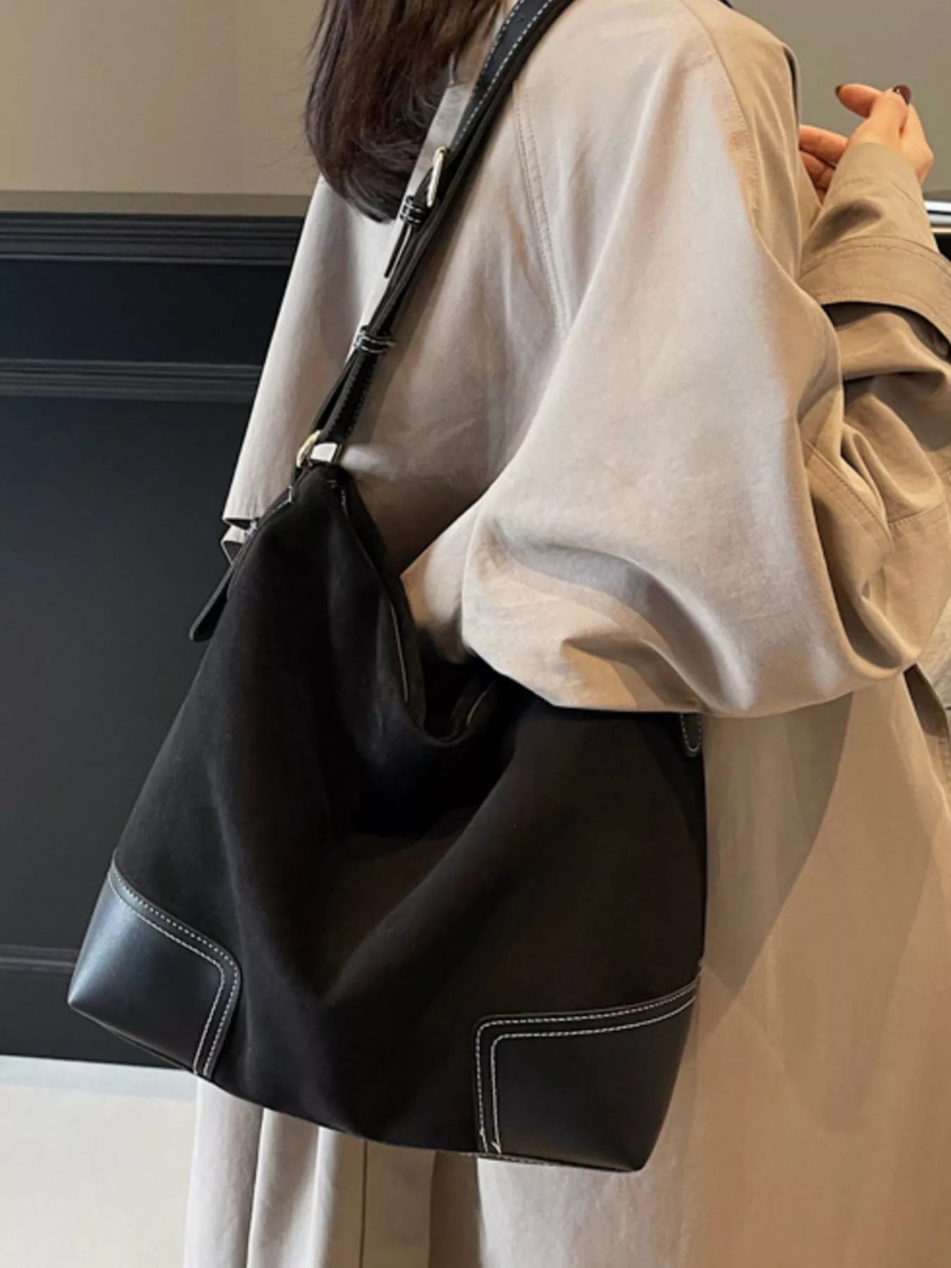 Person wearing a beige outfit with a black shoulder bag indoors.