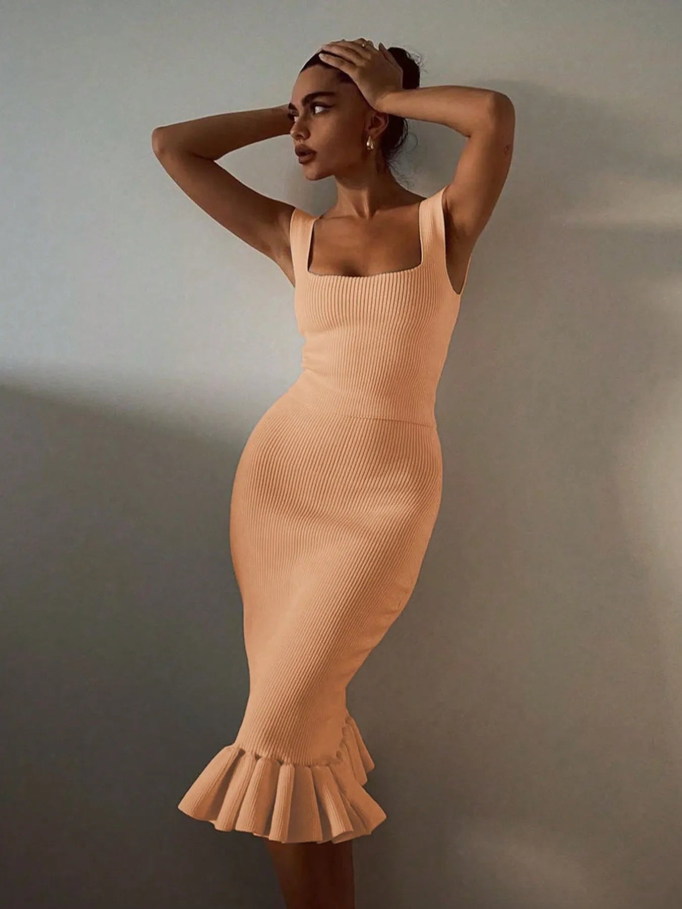 Woman wearing a beige ribbed dress with a ruffled hem against a plain background