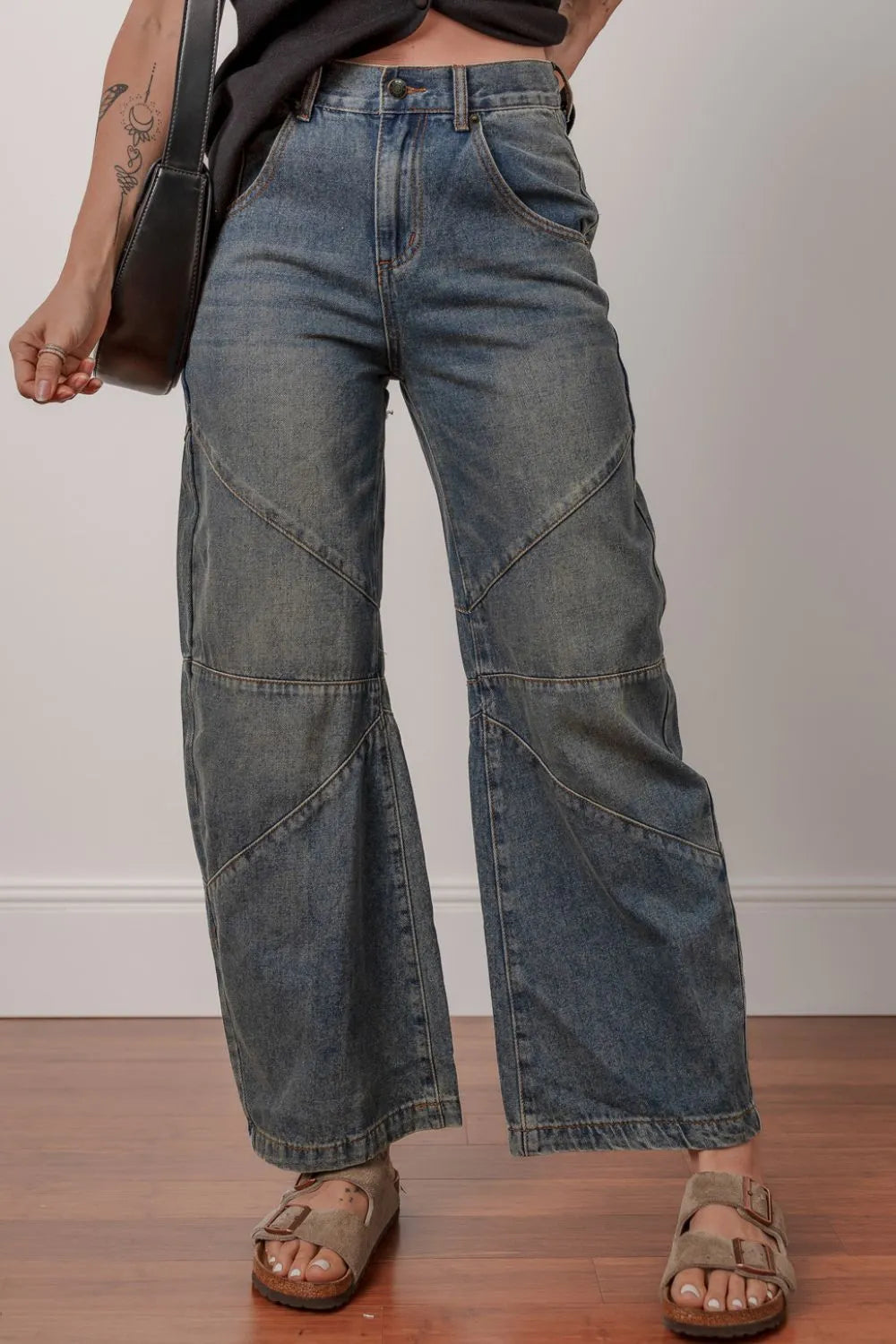 Person wearing wide-leg blue jeans standing on a wooden floor.
