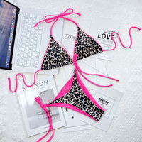 Leopard print bikini with pink straps on a white surface with magazines and a laptop.