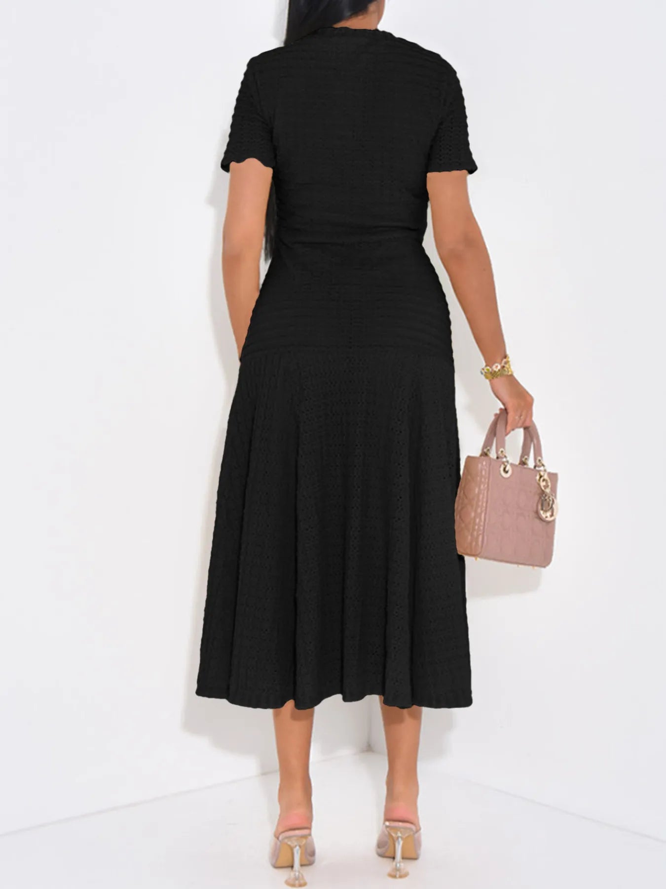 Person wearing a black dress holding a pink handbag on a white background