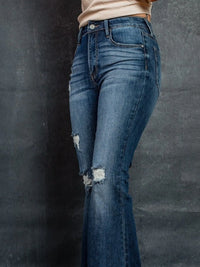 Distressed blue jeans worn by a person against a dark background