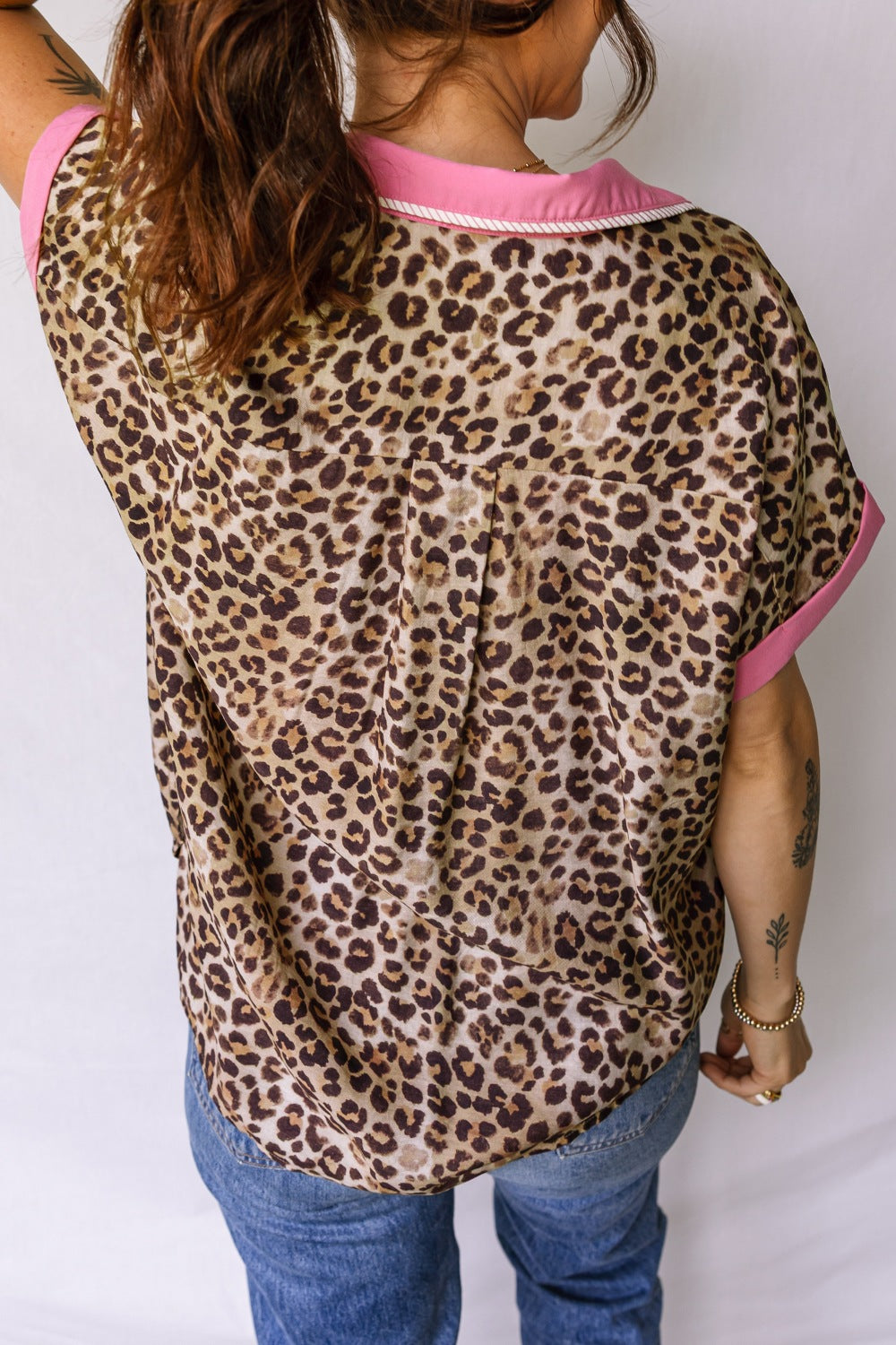 Person wearing a leopard print top with pink trim and blue jeans on a white background