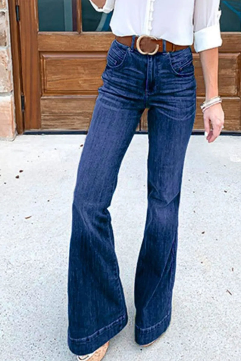 Person wearing blue flared jeans and a white top in front of a wooden door.