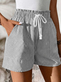 Person wearing gray and white striped shorts with a drawstring on a neutral background
