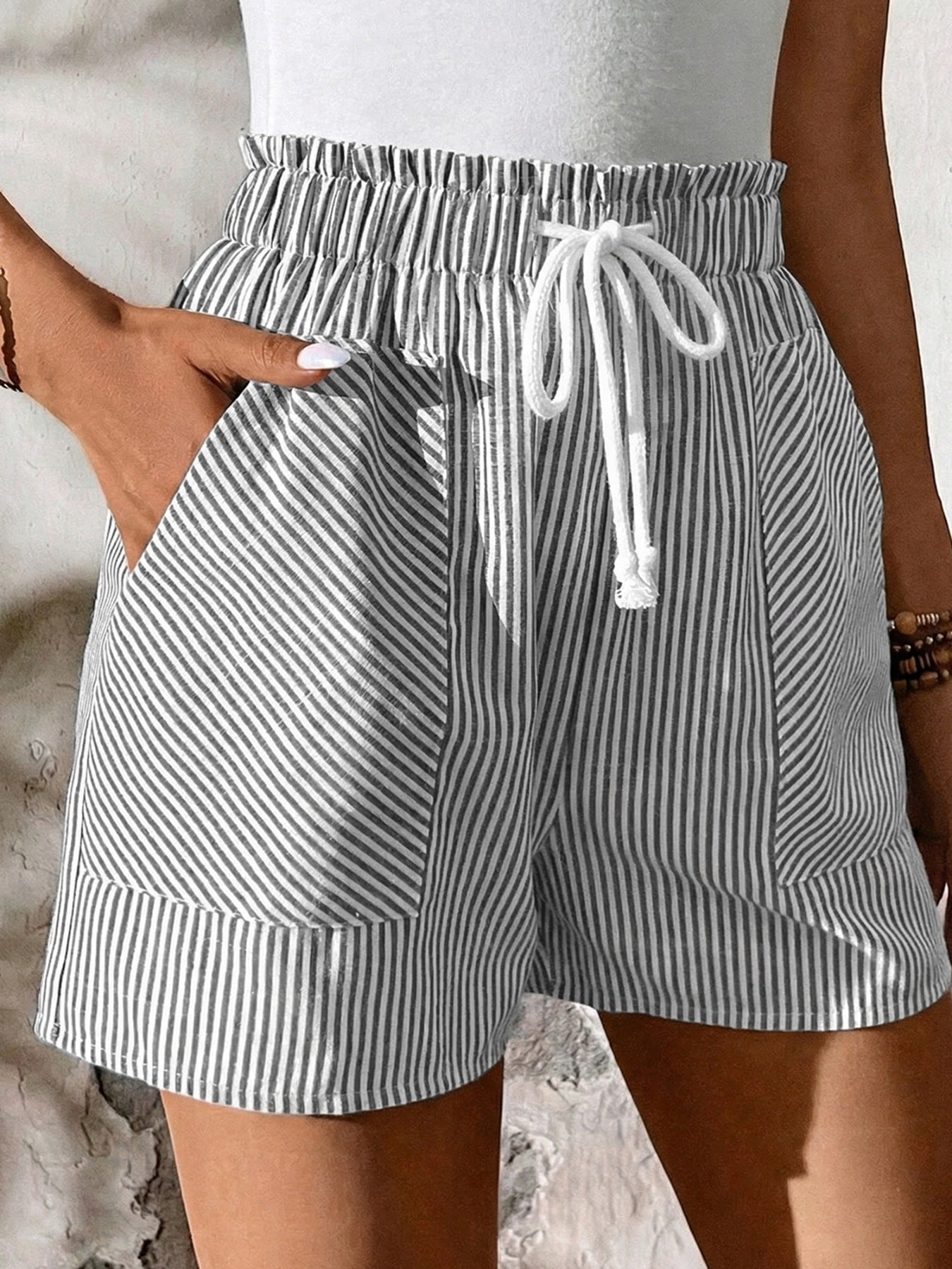 Person wearing gray and white striped shorts with a drawstring on a neutral background