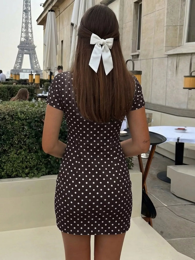 Woman in a polka dot dress with a bow in her hair standing in front of the Eiffel Tower.