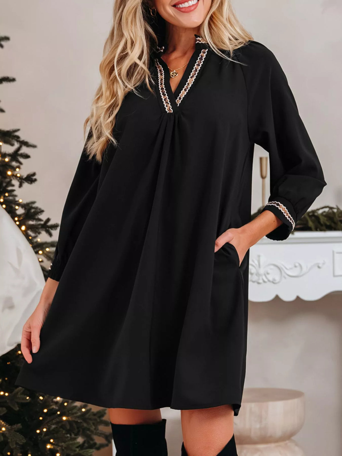 Woman wearing a black dress with decorative trim in a festive indoor setting.